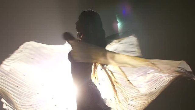 Dancer girl in a white suit hands like wings. Smoke background. Slow motion. Sihouette