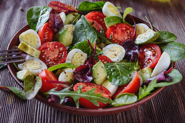 Delicious salad with cherry tomatoes, avocado, herbs, quail egg  pieces in a salad bowl on a wooden table