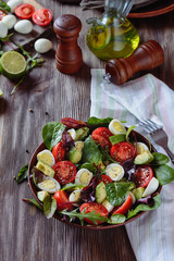Delicious salad with cherry tomatoes, avocado, herbs, quail egg  pieces in a salad bowl on a wooden table