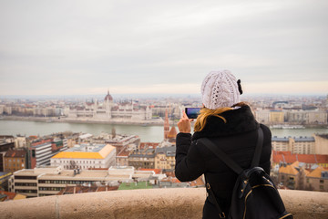 Young woman is taking a photo of Budapest parliament with her smartphone from Fisherman's Bastion in Budapest, Hungary.