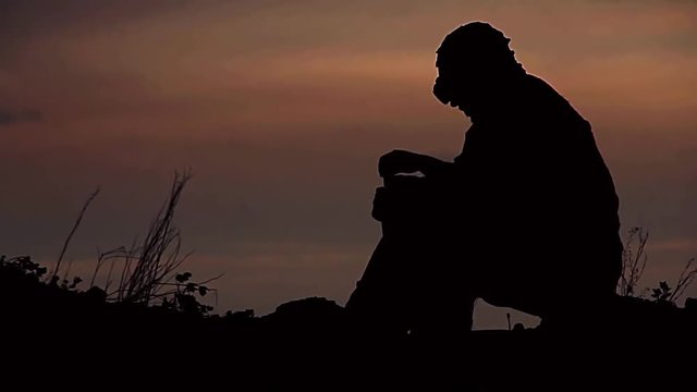 A traveler in a post-apocalyptic world sitting by the fire at sunset. Drink something then go over the hills in the background of a beautiful sunset. Great footage.