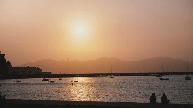 Beautiful romantic sunset panorama of misty San Francisco pier, boats and tourists with Golden Gate bridge in background