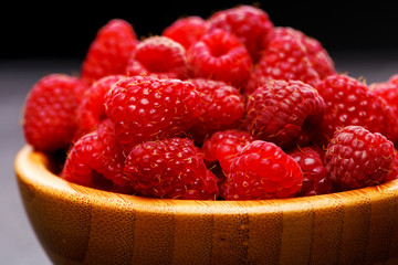 Photo of raspberries in wooden cup on black background