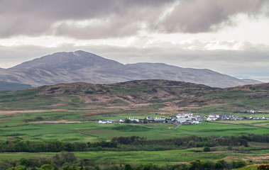 Fototapeta na wymiar A small village on the island of Jura sits beneath large hills and is surrounded by farmland. Viewed from the island of Islay, Scotland.
