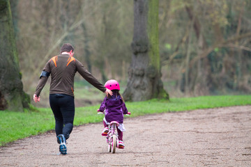 A father runs alongside his daughter who is learning to ride a bike in Shrewsbury, Shropshire, England.