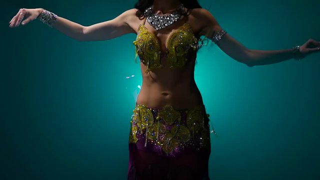 Woman performs a belly dance in oriental costume. Smoke background. Slow motion. Close up
