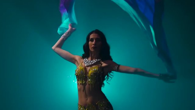 Belly dancer girl dance uses fans. Smoke background. Slow motion. Close up
