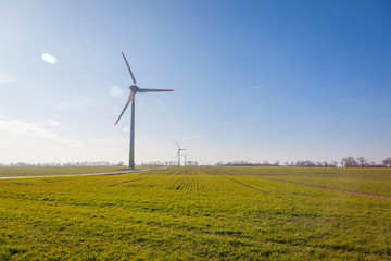 wind turbine on green field with sun flare blue sky background