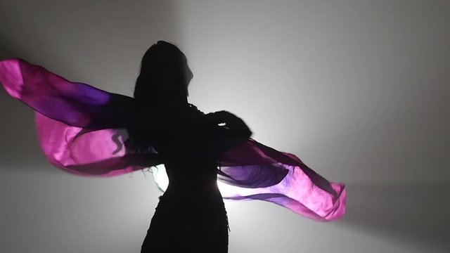 Belly dance with multicolored shawl tarts dancing . Sihouette . Smoke background. Slow motion. Close up