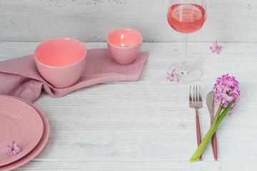 Pink rustic table setting with purple hyacinth flowers, linen napkin, candles and glass of rose wine on white wooden table