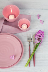 Pink rustic table setting with purple hyacinth flower, candles and linen napkin on white wooden table