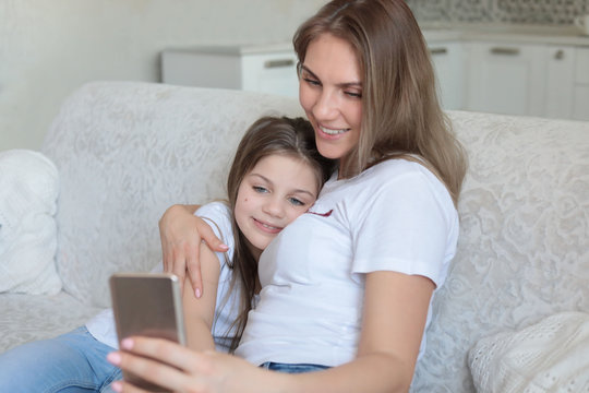 Mom And Daughter Look At The Phone While Sitting On The Sofa At Home, Take A Selfie