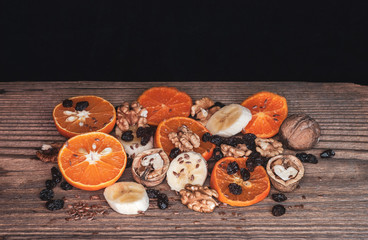 Slices of mandarins and bananas with nuts and raisins on a rustic wooden board. Tasty and healthy snack for everyday.