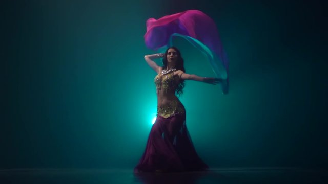 Woman dancing belly dance in dark studio. Smoke background. Slow motion