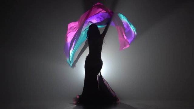 Exotic belly dancer girl continue dance uses fans. Sihouette . Black smoke background. Slow motion