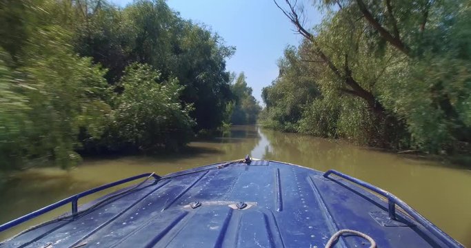 Small blue motor boat sailing on high speed in the narrow channel of Danube river delta at city of Vilkove, Ukraine