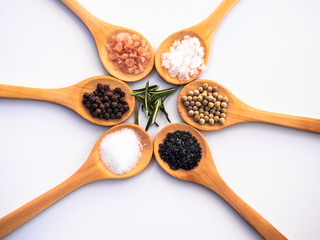 Wooden spoons with himalayan salt, black hawaii salt, common salt, salt flakes, peppercorns and rosemary on a white background