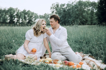 happy man with his pregnant wife at picnic on summer day