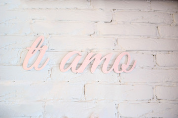 close up photo of hand lettering "ti amo" in pink color on a white brick wall