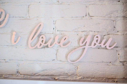 close up photo of hand lettering "i love you" in pink color on a white brick wall
