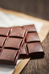 dark chocolate in paper packaging on a wooden table.