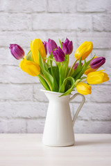 Yellow and purple live tulips in a white jug on a light background