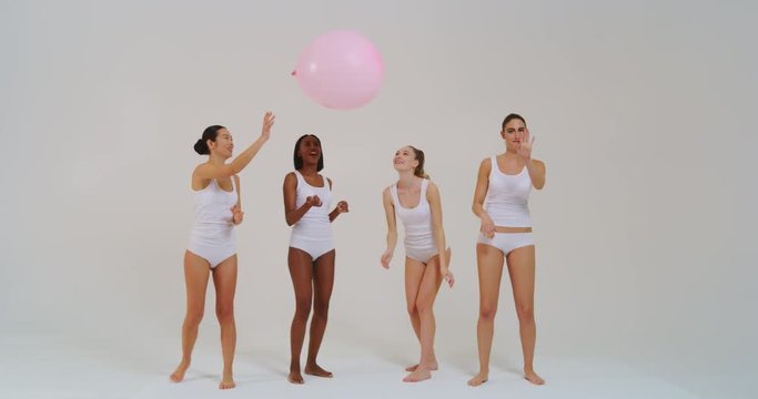 Slow motion  of beautiful young women of different ethnicities with perfect firm and slim body in white tank shirts and panties having fun playing with balloon in baby pink color.