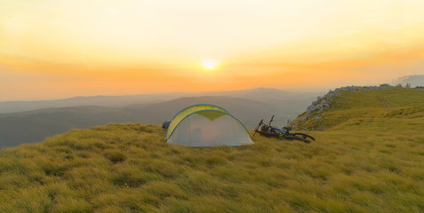 Fototapeta na wymiar AERIAL: Flying behind an empty tent sitting in the meadow at beautiful sunset.