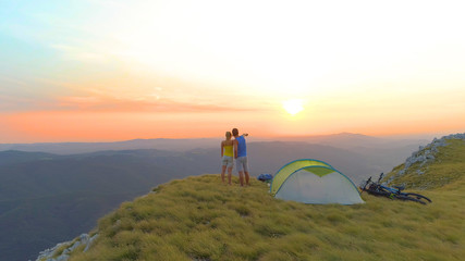 Fototapeta premium AERIAL: Unrecognizable woman and man observing the stunning mountains at sunrise
