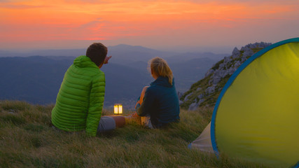 CLOSE UP: Man showing the landscape to girlfriend while sitting by their tent. © helivideo