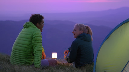CLOSE UP: Cheerful hiker couple talking and laughing while sitting by lantern. © helivideo