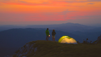 Carefree couple talks by their tent on a cold summer evening in the mountains. © helivideo