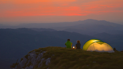 Unrecognizable man and woman sitting by a lantern and talking on a cold morning.
