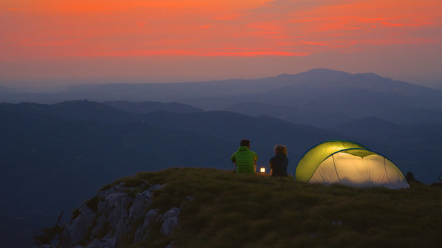 Tourist couple camping in the Alps sit by the lantern and talk on a calm evening