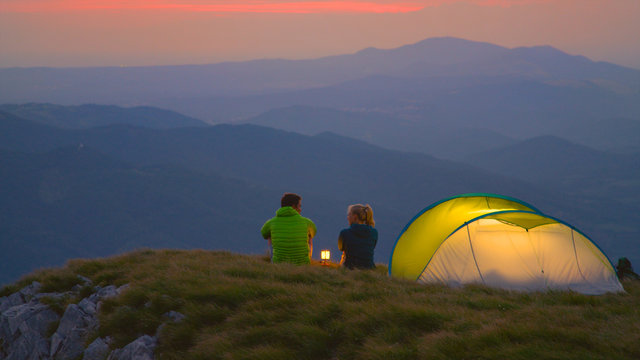 Young hiker couple sitting and talking by the lantern on a cold summer morning