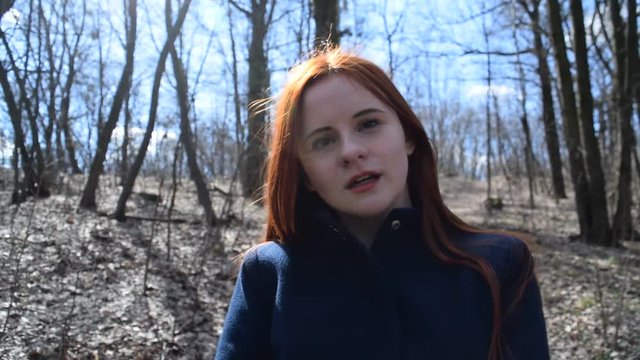 Red-haired young girl in blue coat. Dry forest.