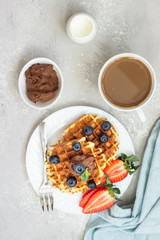 Plate with belgian waffles with chocolate sauce, berries and mint on a light gray background. Breakfast or lunch. Copy space.