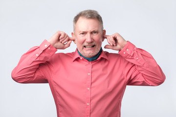 Senior man in red shirt plugging ears with fingers