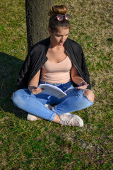 Naklejka na ściany i meble Young woman is reading a book in the city park. Mindfulness, facial expression, emotions. Education and lifestyle