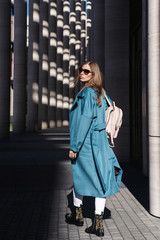 Young beautiful stylish woman walking in blue coat, white jeans and black shoes, holding pink bag in hands, street style, spring summer trend. Fashion season shopping concept