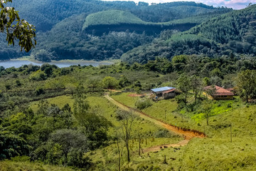 Paisagem em vale com montanha ao fundo,  estrada de terra, casa e rio