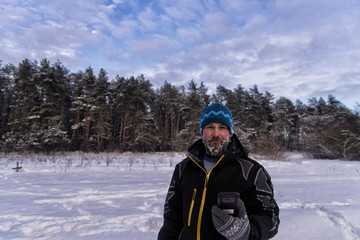 Fototapeta na wymiar Good-natured bearded man with a snowy beard, slight smile and GPS navigator is standing on the edge of a taiga forest