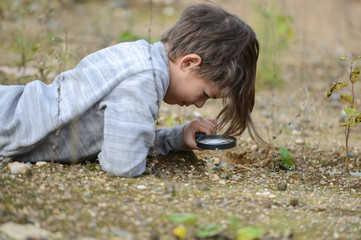 a boy in nature sitting on the ground looking at a magnifying glass plants