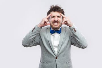 headache. Portrait of sick or worry bearded man in casual grey suit and blue bow tie standing and...