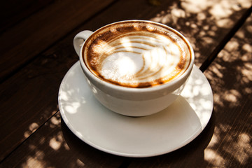 Close up white coffee cup with heart shape latte art foam on black wood table