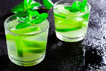 Summer drink Mojito, with lime and mint, on a black background with water drops.