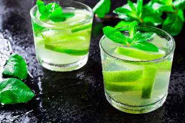 Summer drink Mojito, with lime and mint, on a black background with water drops.