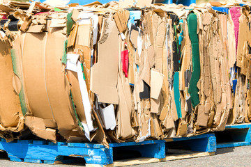 Bundles of cardboard to be recycled. Cardboard is bundled into bales. Scene is outdoors on a sunny...
