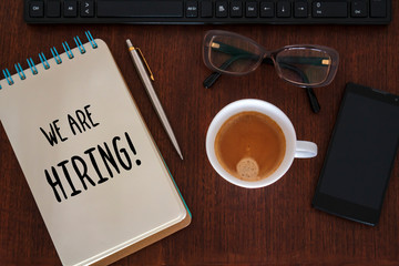 Top view of desk with office accessories and We are hiring text written on notebook