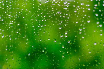 Small raindrops on the window glass in the summer against the backdrop of green